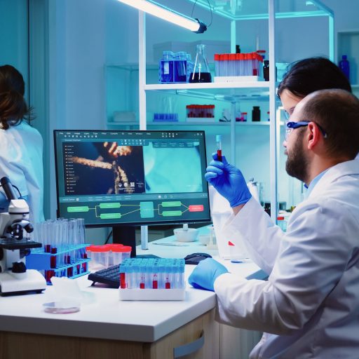 Microbiologist doctor taking a blood sample tube from rack Microbiologist doctor taking a blood sample tube from rack with machines of analysis in the lab background. Doctors examining vaccine evolution using high tech researching diagnosis against covid19