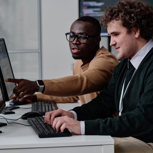 Programmers working with computer program in team Programmer pointing at computer monitor with codes and talking to his colleague while they working with computer program in team